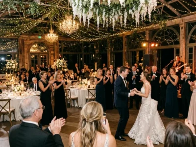 Bride and groom dancing in a candlelit barn venue under fairy lights while guests clap and a live band plays